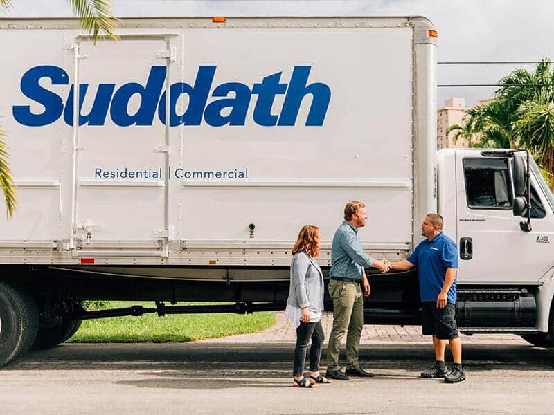 couple shaking hands with mover in front of moving truck