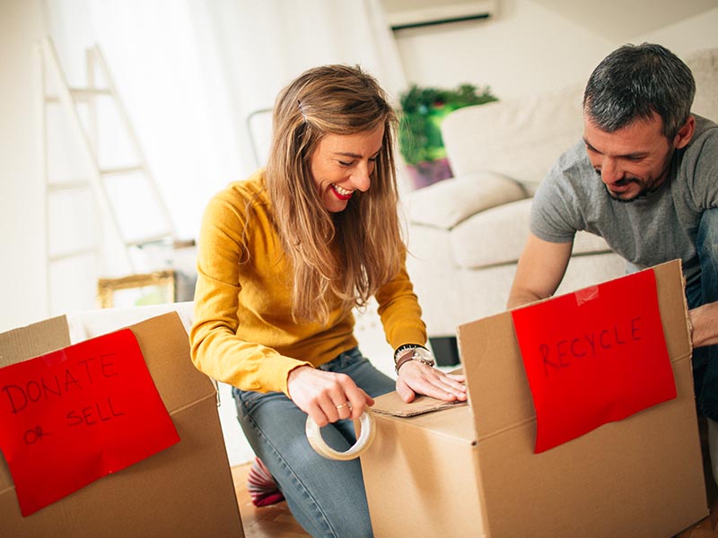 smiling couple taping boxes of items to donate and recycle